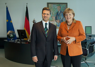 meeting between: Angela merkl enrique pena nieto. photo shows them both standing in Angelas office, her desk is in the background, a german flag is on the left side of the desk.